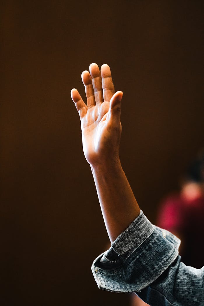 A hand raised in worship indoors, capturing a moment of faith and devotion.